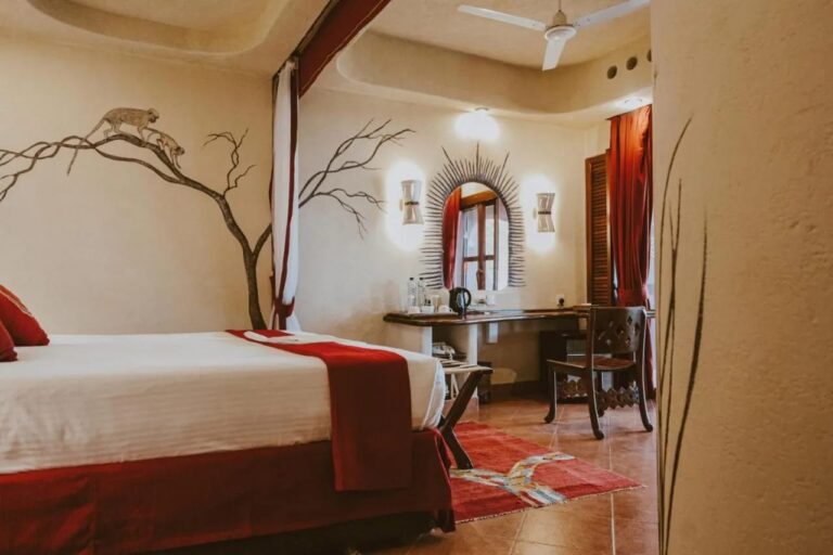 Ein Zimmer mit einem Baum und zwei Affen an der Wand, dazu ein Schreibtisch unter einem Sonnenspiegel