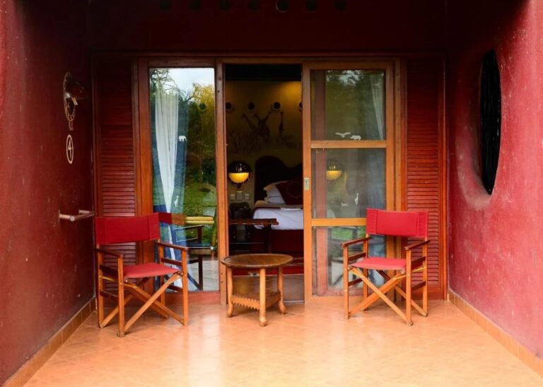 Die Terrasse eines Zimmers zwischen zwei roten Mauern, mit zwei roten Klappstühlen und einem runden Tisch