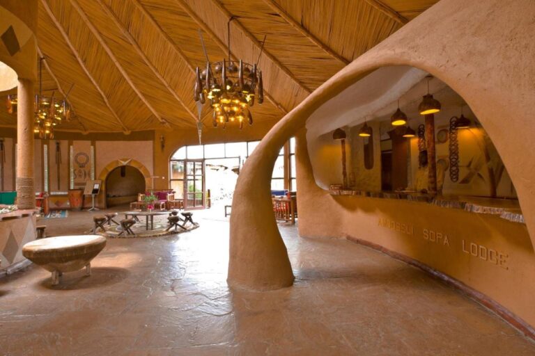 Der Empfangstresen aus geformtem Lehm mit dem eingravierten Namen der Amboseli Sopa Lodge, unter einer Schilfdecke