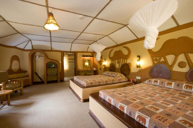 Ein Zimmer mit zwei Betten, mit einem Büffelkopf und einem Elefanten als Relief an der Wand