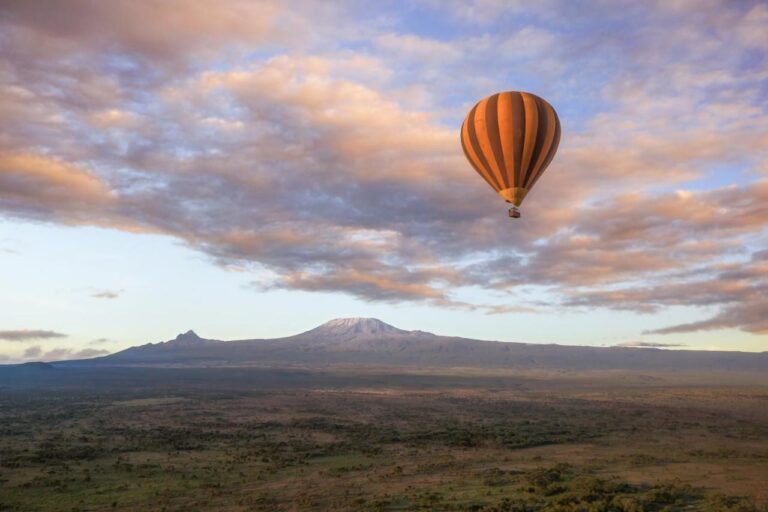 Ein Heißluftballon über der Ebene, am Horizont der Kilimandscharo unter rosa Himmel