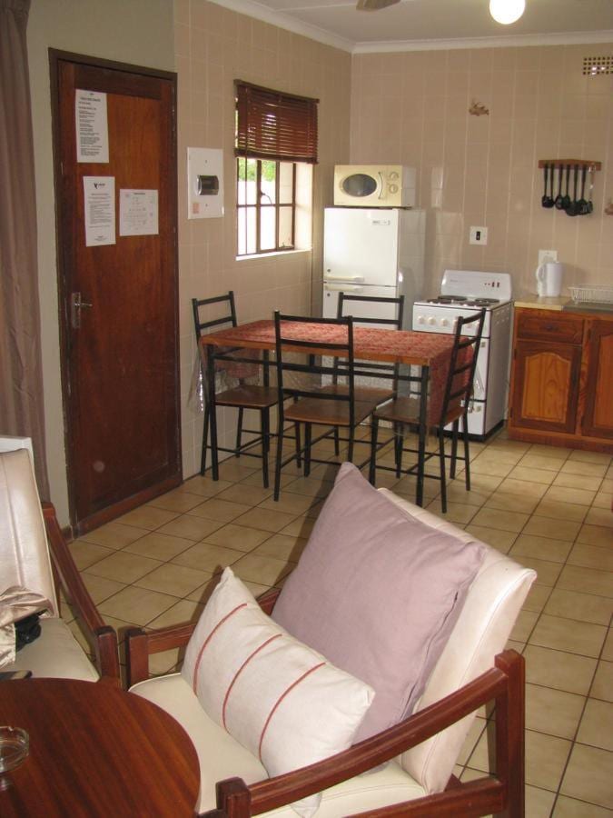 Die Küchenecke eines Chalets mit Esstisch, Kühlschrank und Mikrowelle, von einem Sessel mit rosa Kissen aus gesehen
