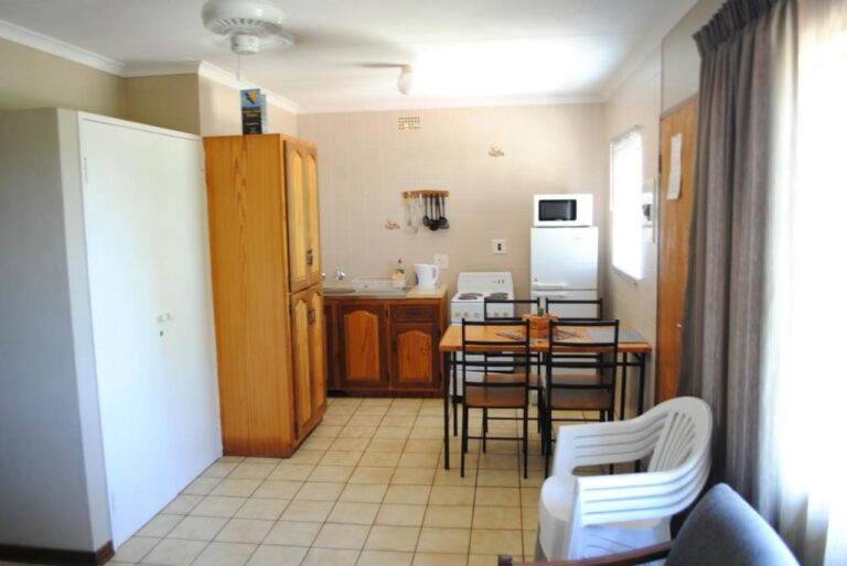 Der Wohnraum eines Chalets mit Küchenecke, Esstisch, Holzschrank und weißem Stuhl