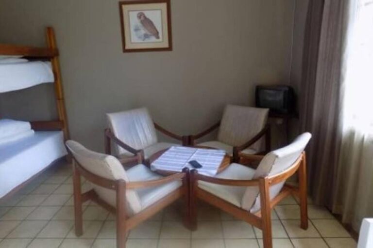 Vier Sessel mit weißen Kissen um einen Couchtisch, neben einem Etagenbett, unter einem Eulenbild