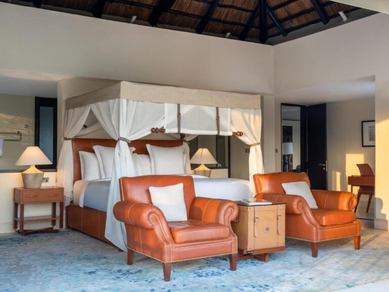 Ein Zimmer mit Himmelbett und zwei orangefarbenen Ledersesseln
