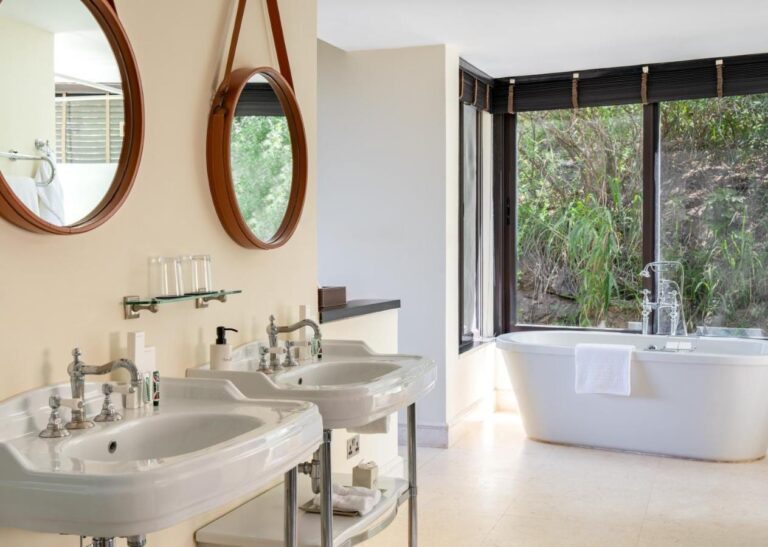 Ein Bad mit zwei Standwaschbecken, runden Spiegeln und einer Badewanne vor einer Fensterfront