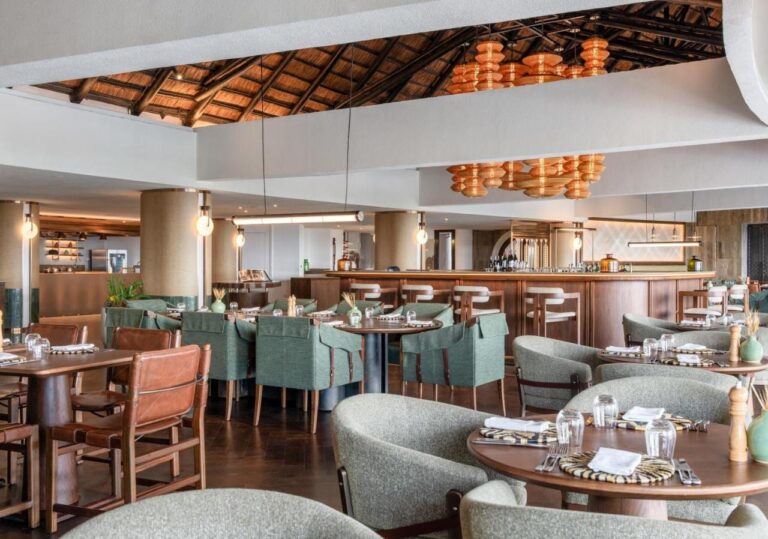 Ein Restaurant mit grünen Sesseln vor einer langen Bar, unter orangefarbenen Hängeleuchten