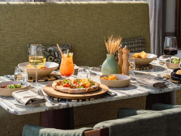 Eine Pizza, Salate, ein Cocktail und zwei Gläser Wein auf einem Marmortisch