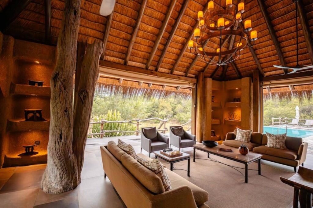 Die Lounge der Kapama River Lodge unter einem hohen Strohdach, offen zu einem Pool und zum Busch