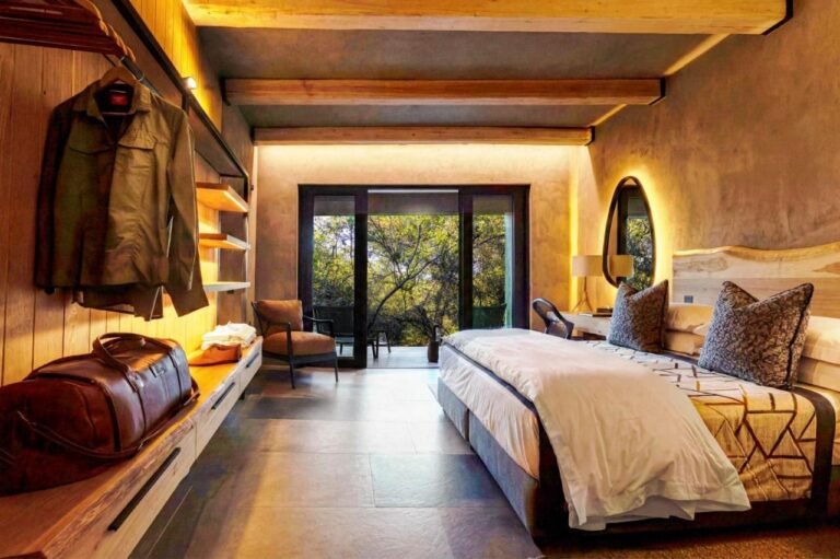 Eine aufgehängte Jacke und eine Reisetasche in einer Suite, gegenüber dem großen Bett und der Terrasse