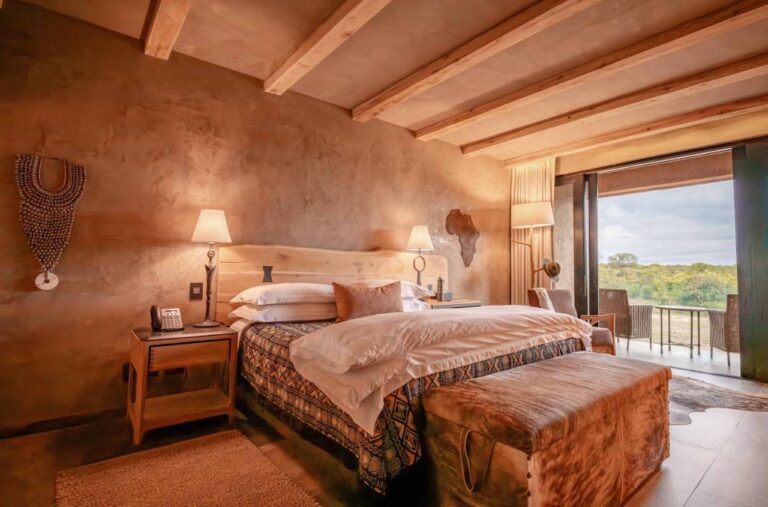 Eine Suite mit großem Bett, einer Afrikakarte aus Holz an der Wand und einer Terrasse zum Busch