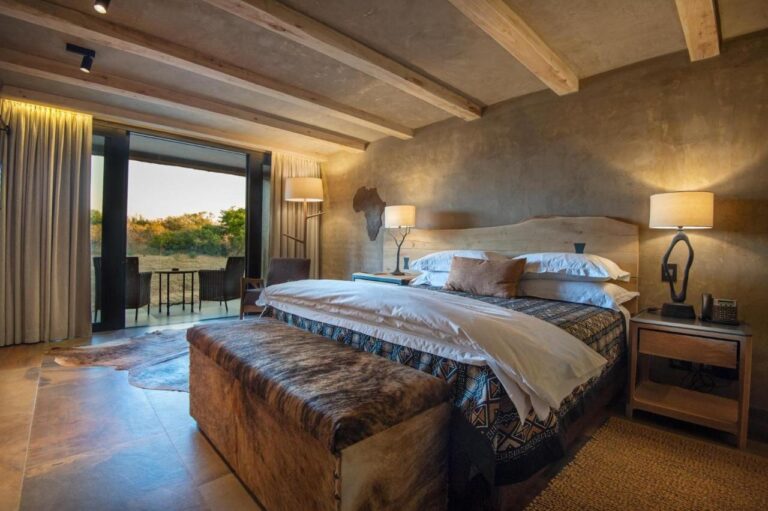 Eine Suite mit großem Bett, einer Fellbank am Fußende und einer möblierten Terrasse mit Blick auf den Busch