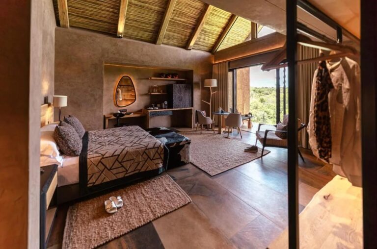 Eine Suite der Kapama River Lodge unter einem Dachstuhl aus Holz und Stroh, mit Schreibecke und Blick auf die Bäume