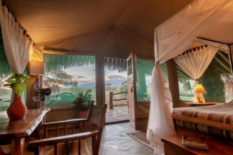 Ein Zelt des Kibo Safari Camps, offen zur Terrasse, in der Ferne der Kilimandscharo in der Abenddämmerung