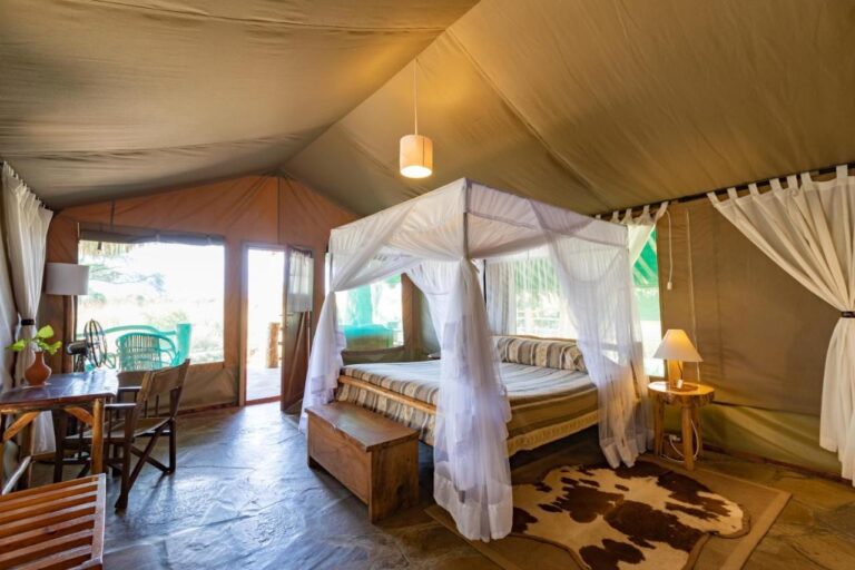 Ein Zelt mit einem Bett unter einem Moskitonetz, einem Schreibtisch und einer offenen Tür zur Terrasse