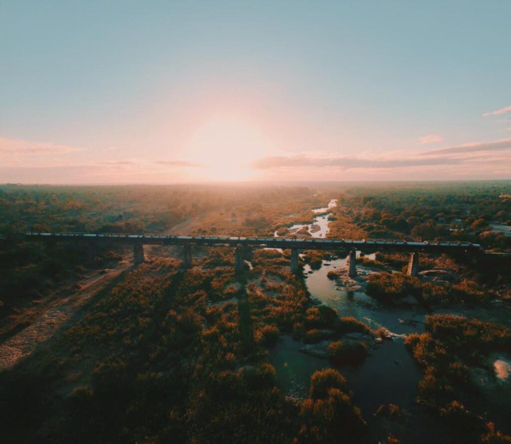 Der Zug des Kruger Shalati auf der Selati-Brücke aus der Luft, über dem Fluss und dem Busch, die Sonne tief am Horizont