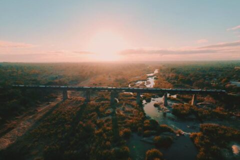 Der Zug des Kruger Shalati auf der Selati-Brücke aus der Luft, über dem Fluss und dem Busch, die Sonne tief am Horizont