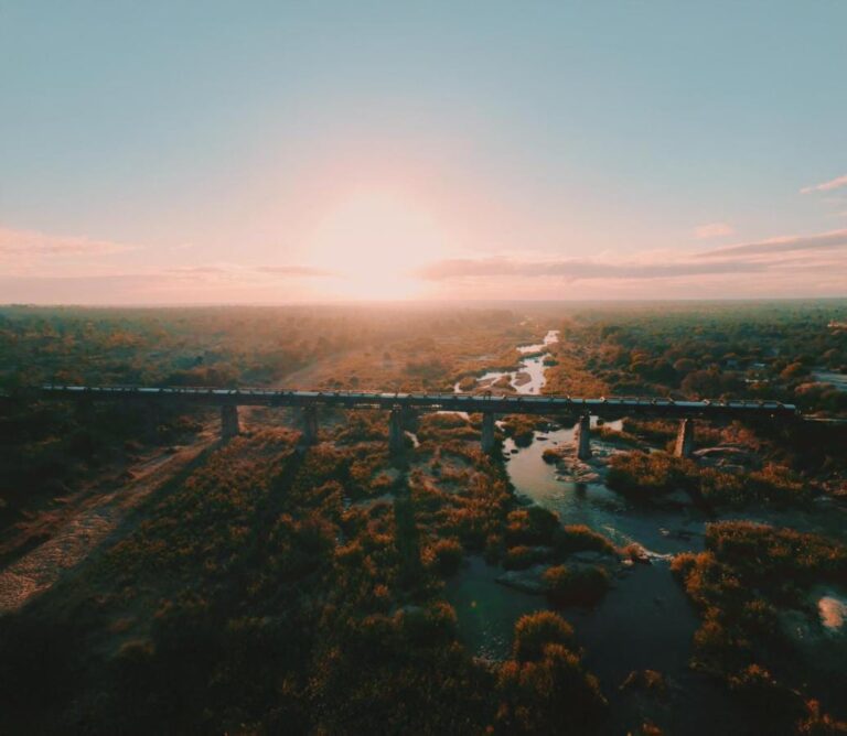 Der Zug des Kruger Shalati auf der Selati-Brücke aus der Luft, über dem Fluss und dem Busch, die Sonne tief am Horizont