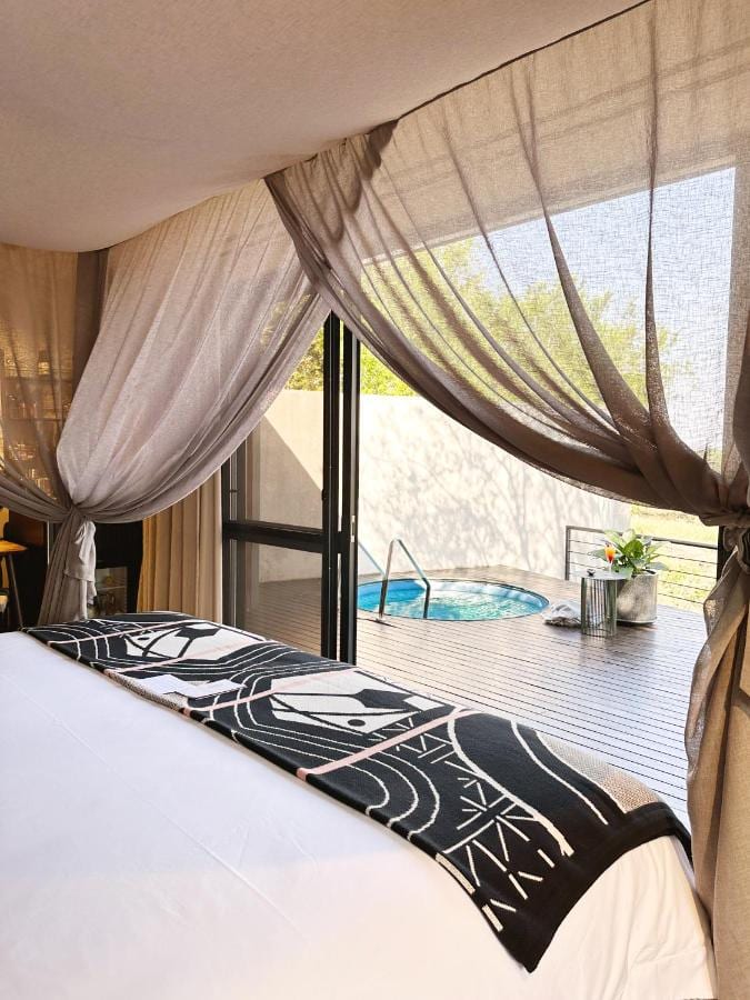 Eine Gartensuite, das Bett unter Schleiervorhängen, offen zu einer Holzterrasse mit kleinem runden Pool