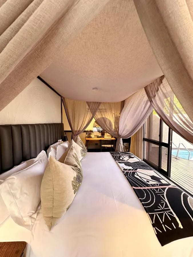 Das große Bett einer Suite unter Schleiervorhängen, mit dem kleinen Pool hinter der Fensterfront