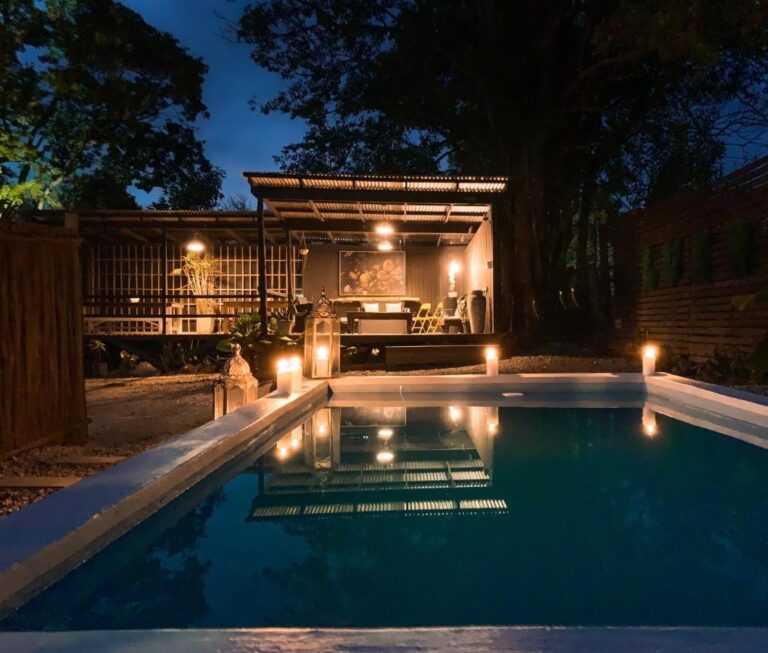Der Pool des Lush bei Einbruch der Dunkelheit, von Kerzen beleuchtet, vor einer überdachten Terrasse mit Blechdach