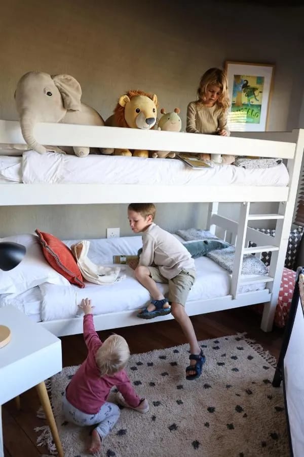 Drei Kinder spielen um ein Etagenbett, mit einem Plüschelefanten und einem Plüschlöwen