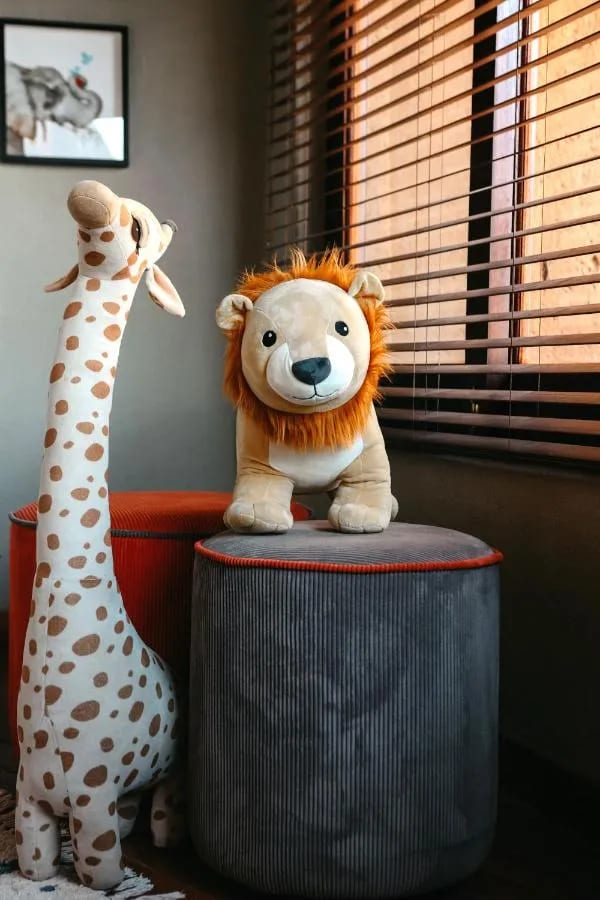 Eine Plüschgiraffe und ein Plüschlöwe an einem Fenster mit Jalousien