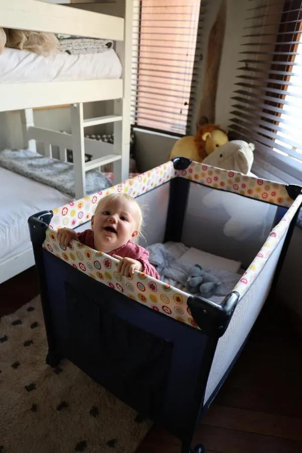 Ein lächelndes Baby in einem Reisebett, vor den Etagenbetten
