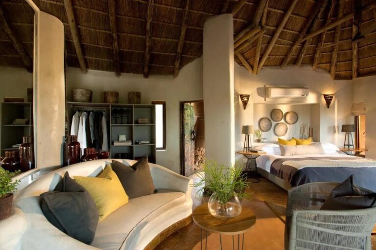 Eine Suite der Madikwe Safari Lodge mit rundem weißem Sofa, großem Bett und offenem Kleiderschrank