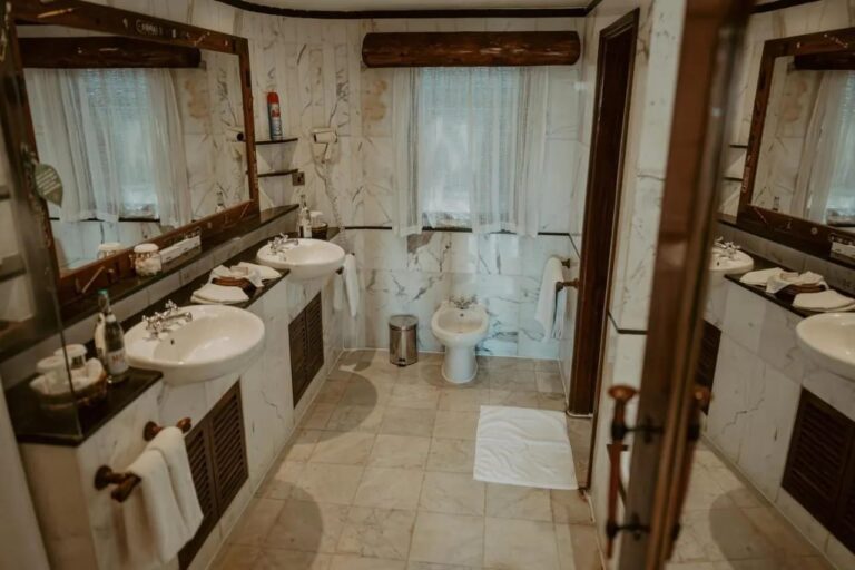 Ein Bad aus weißem Marmor mit zwei Waschbecken, einem Wandföhn und einem Bidet unter dem Fenster