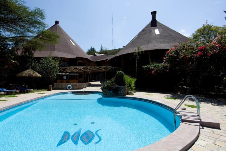 Der Pool der Mara Sopa Lodge vor Gebäuden mit großen kegelförmigen Strohdächern