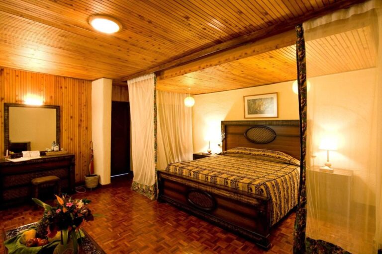 Ein Zimmer mit holzverkleideter Decke, großem Himmelbett und Frisiertisch