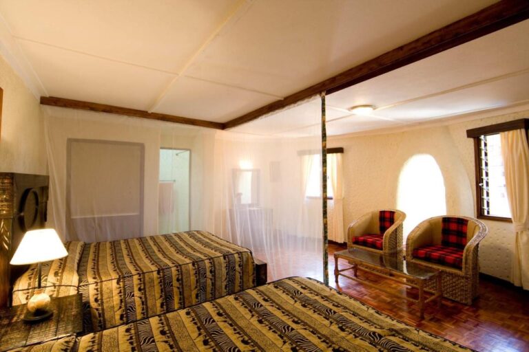Ein Zimmer mit zwei Betten unter Moskitonetzen und zwei Sesseln mit rot karierten Kissen