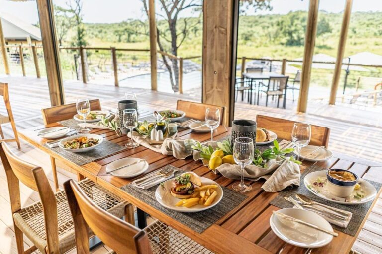 Ein gedeckter Tisch im Restaurant, offen zur Terrasse, zum Pool und zum Busch