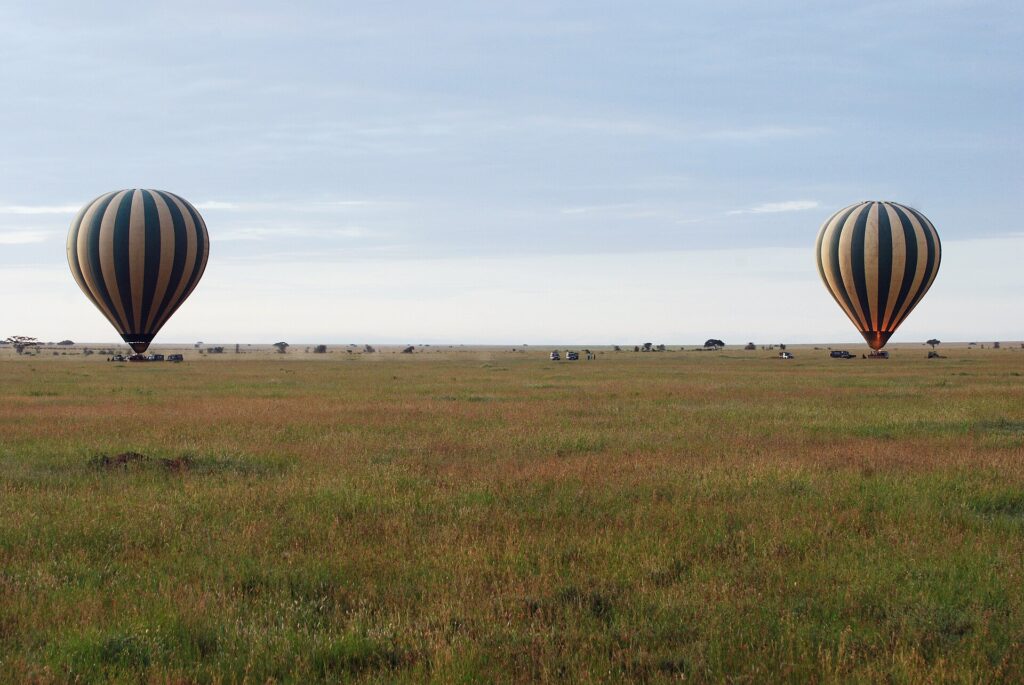 Zwei gestreifte Heißluftballons landen am frühen Morgen in der grünen Ebene, gefolgt von den 4x4