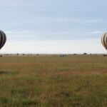 Zwei gestreifte Heißluftballons landen am frühen Morgen in der grünen Ebene, gefolgt von den 4x4