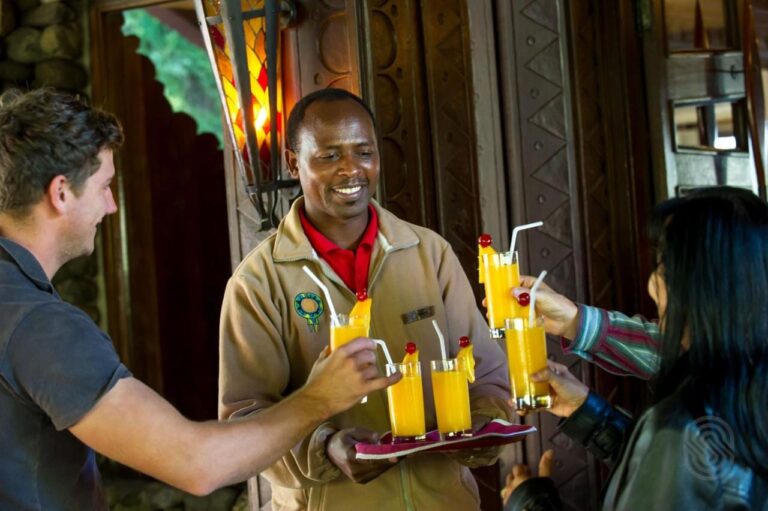 Ein Mitarbeiter der Ngorongoro Serena Safari Lodge reicht zwei Reisenden ein Tablett mit Fruchtsäften