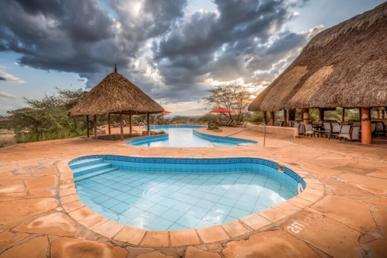Ein kleines gefliestes Becken im Vordergrund und der große Pool der Samburu Sopa Lodge, zwischen einer Strohhütte und einer Terrasse mit Strohdach