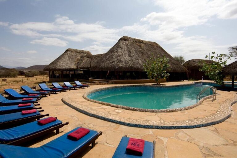 Blaue Liegestühle mit roten Handtüchern am Pool, vor Gebäuden mit Strohdach