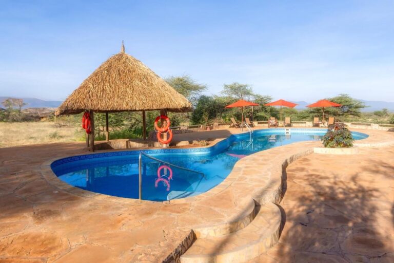 Der Pool der Samburu Sopa Lodge, seine Strohhütte mit orangefarbenen Rettungsringen und rote Sonnenschirme mit Blick auf den Busch