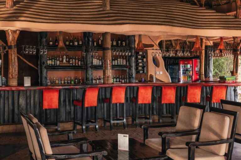 Die Bar mit roten Hockern und Flaschenregalen, im Vordergrund Sessel