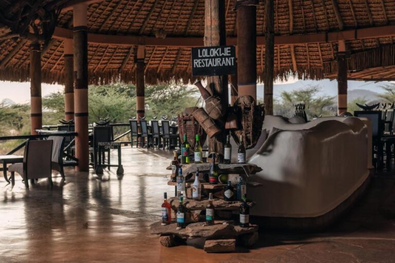 Der Eingang des Restaurants Lolokwe, mit Weinflaschen auf Steinen, unter einem großen Strohdach