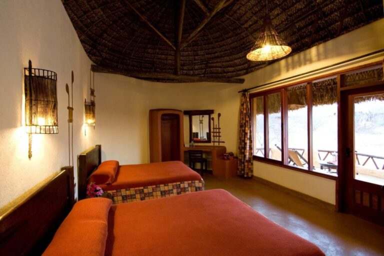 Ein Zimmer mit zwei Betten mit orangefarbenen Tagesdecken und großen Fenstern zur Terrasse
