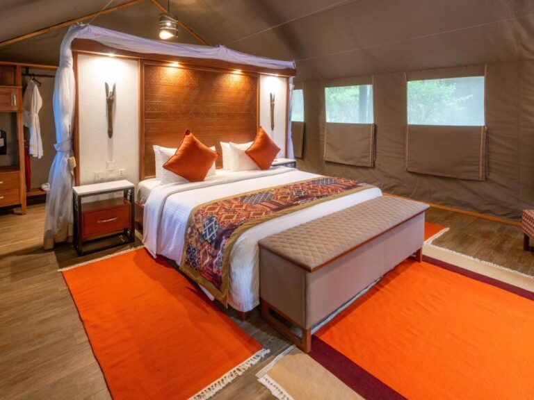 Ein Zelt mit großem Bett unter Moskitonetz, orangefarbenen Kissen und einer Bank am Bettende