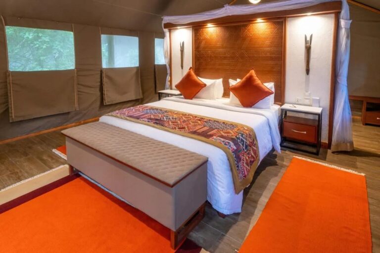 Das Bett eines Zelts schräg von der Seite, mit hölzernem Kopfteil und orangefarbenen Teppichen
