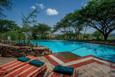 Der Infinity-Pool der Serengeti Serena Safari Lodge mit rot gestreiften Liegestühlen und grünen Handtüchern, unter Akazien