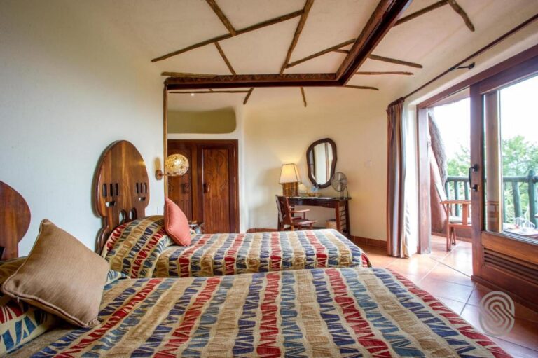 Ein Zimmer mit zwei Betten mit ausgesägten Holzkopfteilen, durch eine Glastür offen zu einem Balkon