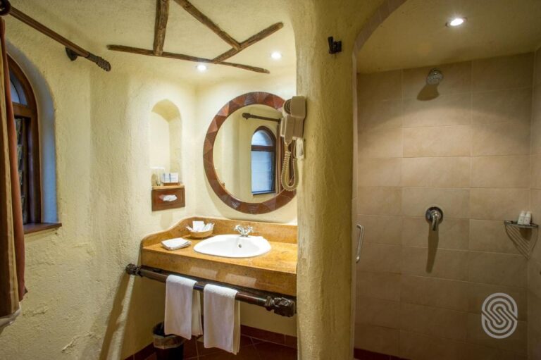 Ein Bad mit verputzten Wänden, einem Waschbecken unter rundem Spiegel und einer großen gefliesten Dusche
