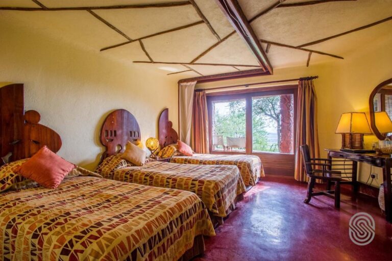 Ein Zimmer mit drei Betten mit geschnitzten Holzkopfteilen, auf einem roten, gewachsten Boden