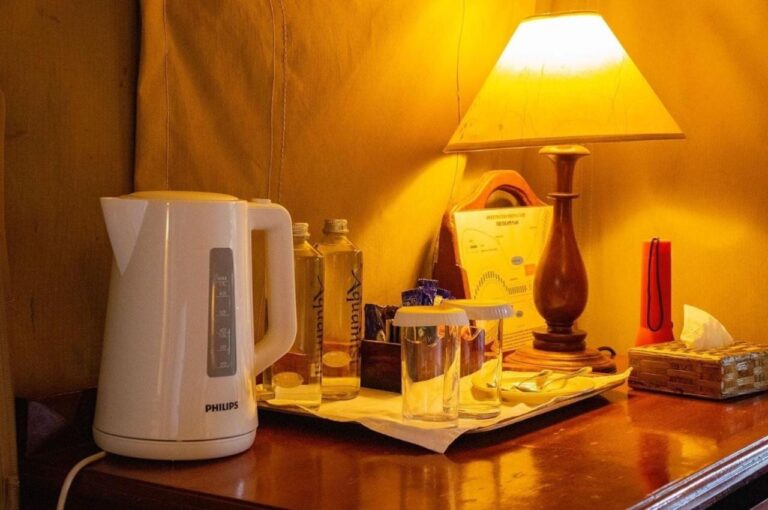 Ein Wasserkocher, Wasserflaschen und Gläser auf einem Schreibtisch, unter einer Lampe